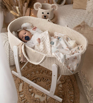 Baby in a cream crochet moses basket with a white wooden stand